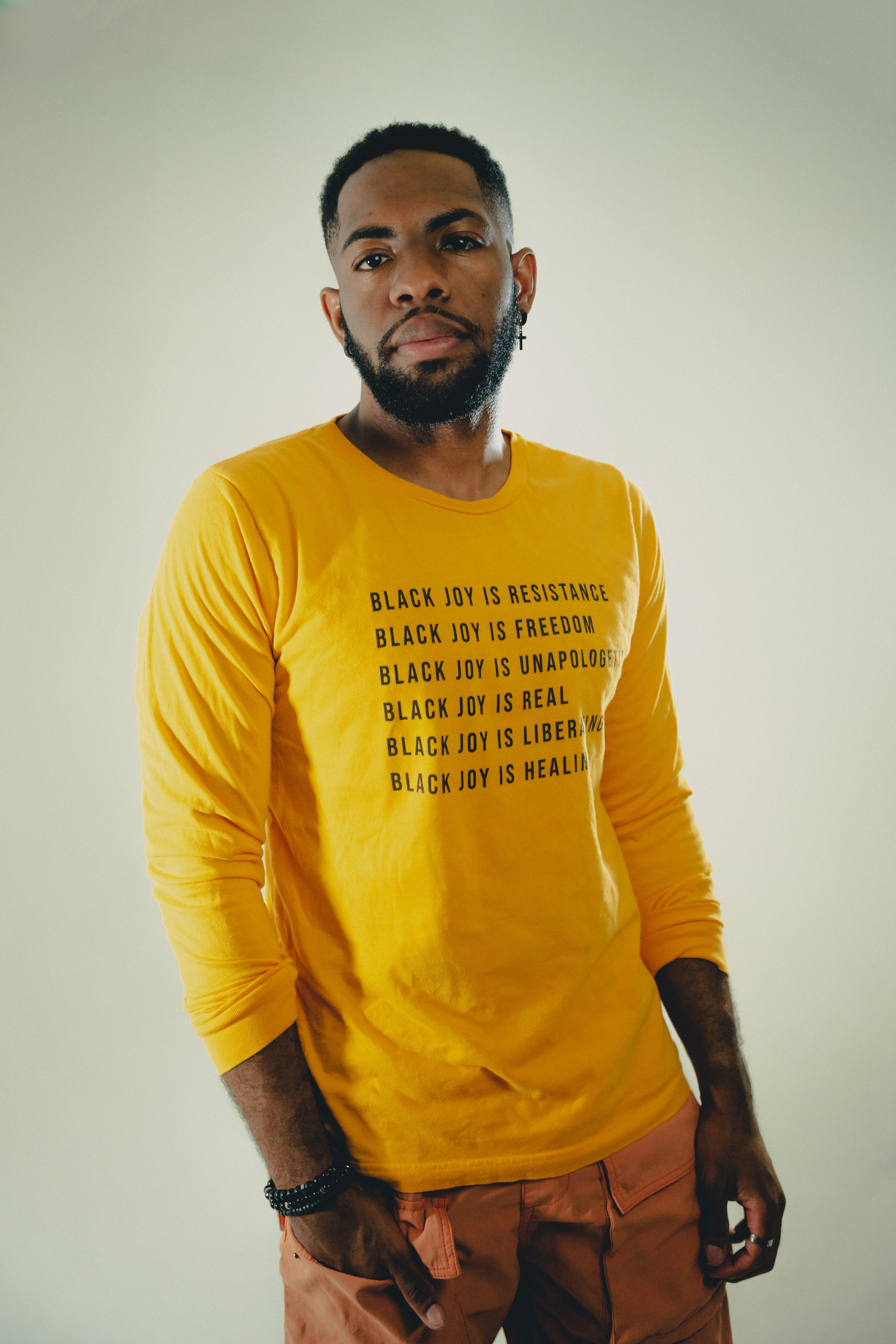 Fashion portrait of a man posing confidently in a yellow shirt with 'Black Joy' text.