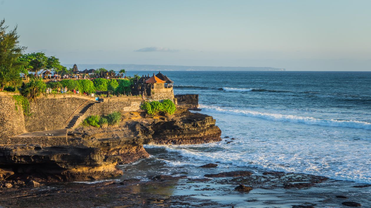 Aerial view of Tanah Lot Temple in Bali surrounded by ocean waves and rocky shores