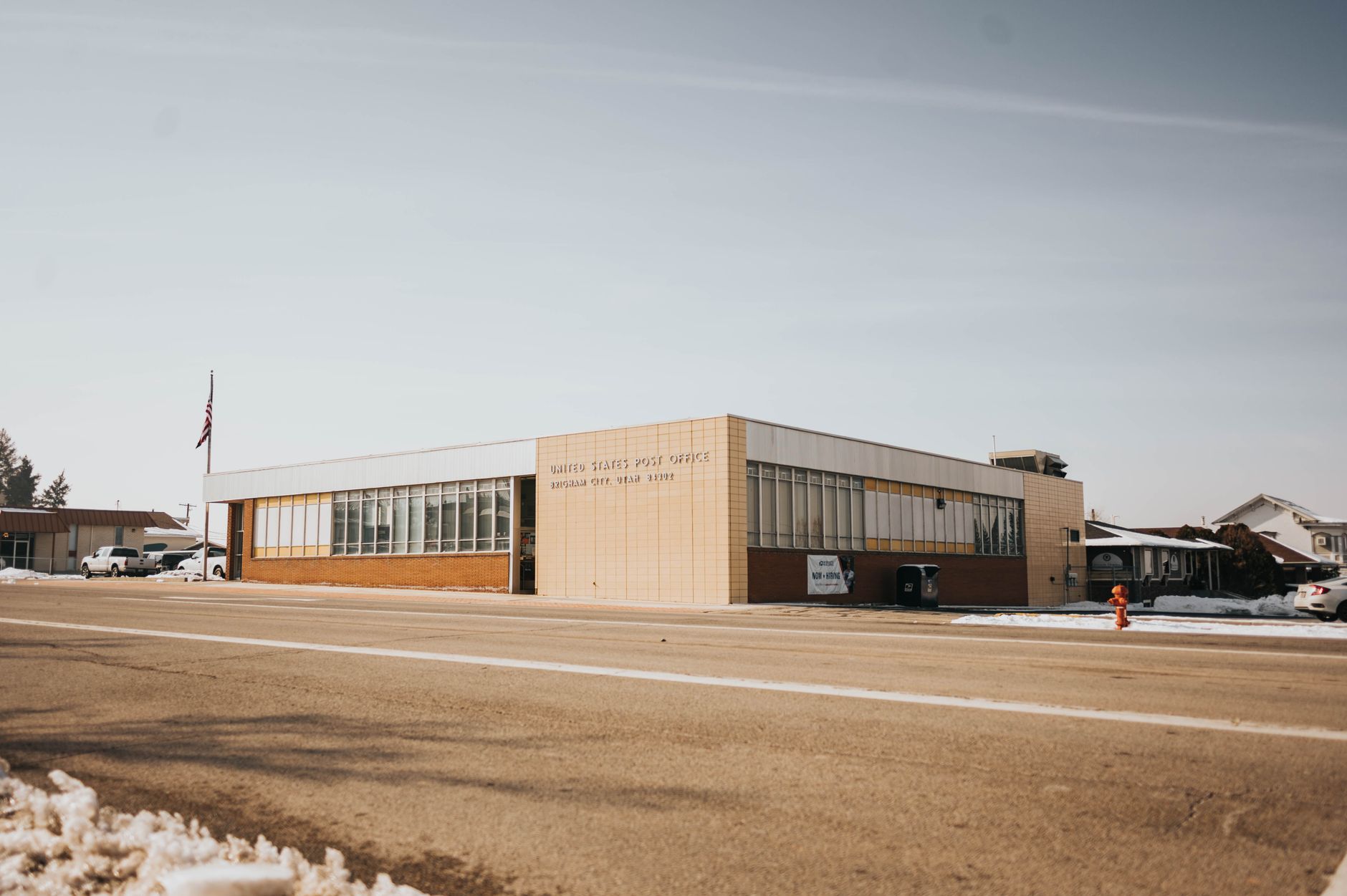 A tranquil view of a United States Post Office during winter with snow, clear sky, and urban surroundings.