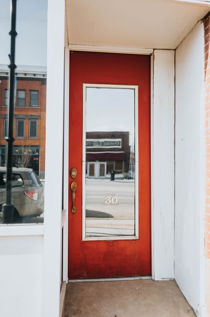 A striking red door in a city scene with reflections of urban architecture.