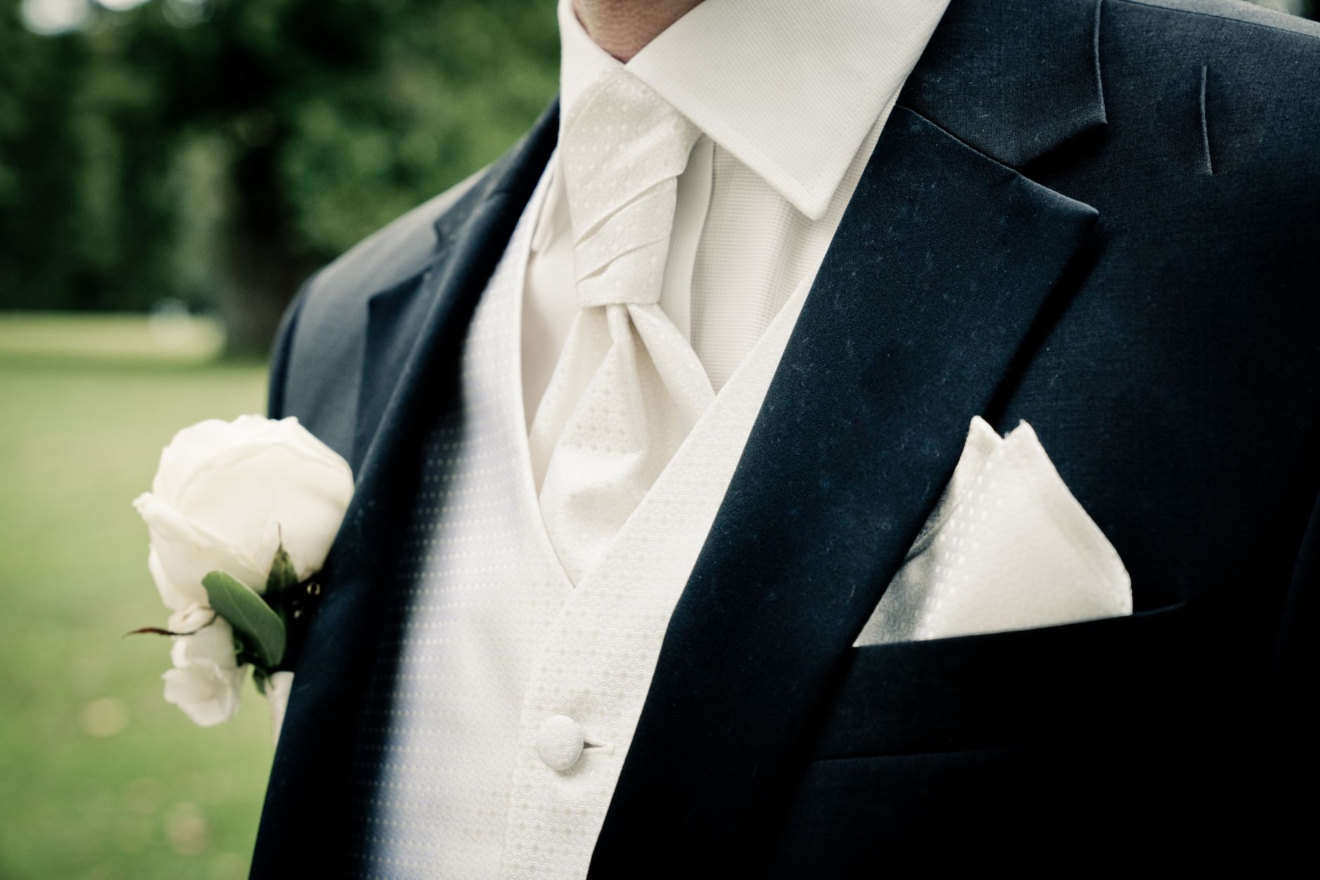 Close-up of groom's suit and tie with white rose boutonniere, symbolizing wedding elegance.