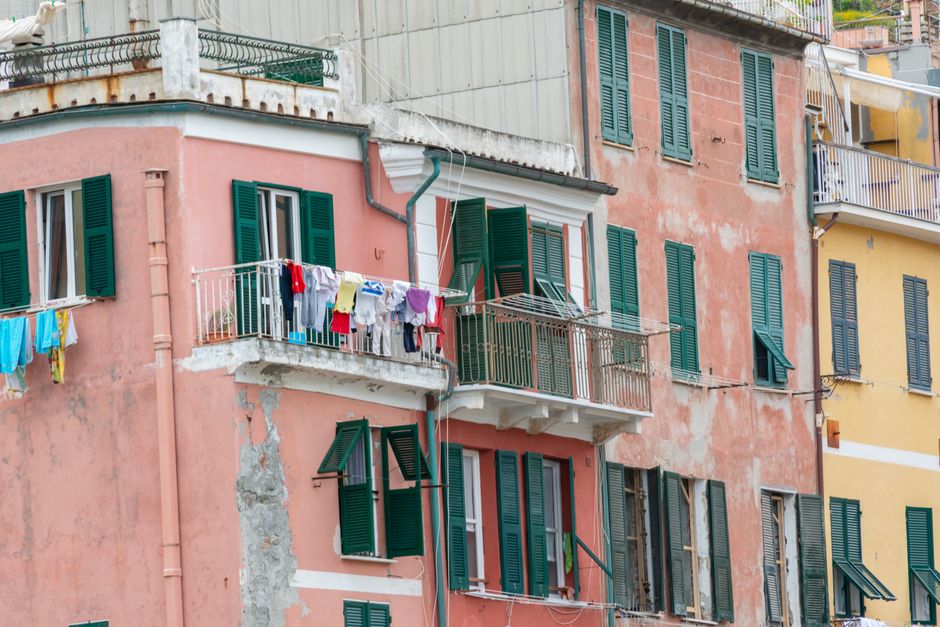 Weathered Mediterranean building facade with peeling pink plaster, green shutters and laundry drying on a balcony.