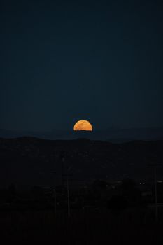 A captivating nighttime view of the full moon rising over a dark mountain landscape.