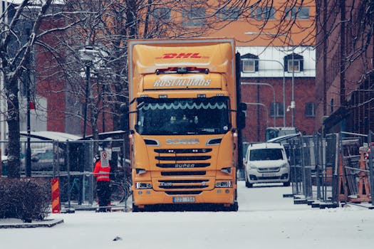 A yellow truck among snowy urban streets, surrounded by buildings and winter scenery.