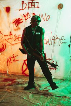 Energetic musician with dreadlocks in an urban setting, holding an electric guitar. Graffiti in background.