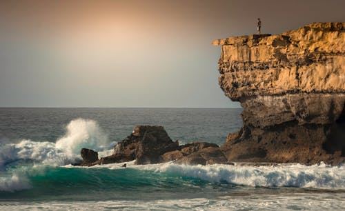 Free Человек, стоящий на вершине скалы в окружении моря Stock Photo