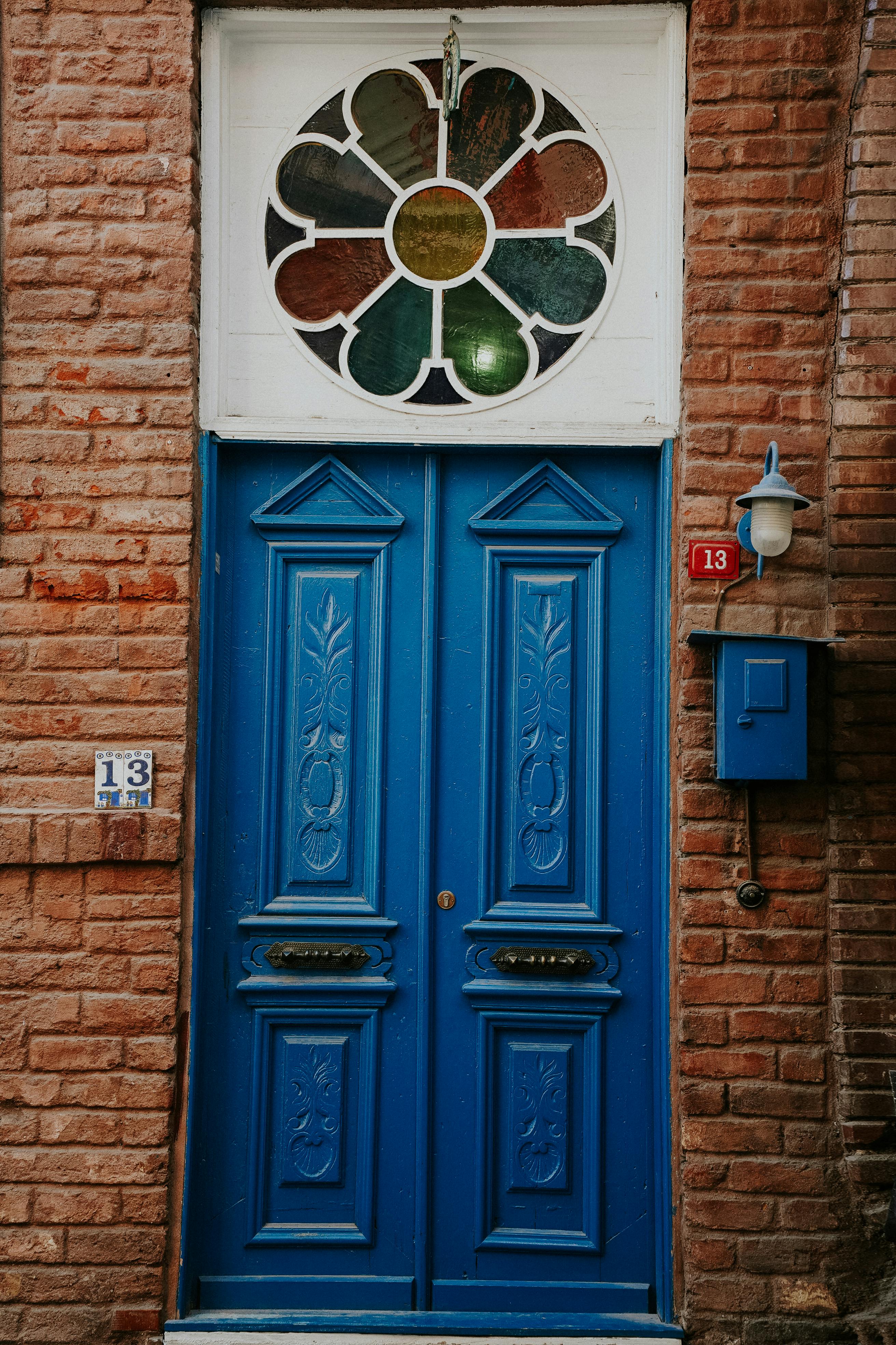A vibrant blue door featuring intricate carvings and a stained glass window, set in a brick wall.