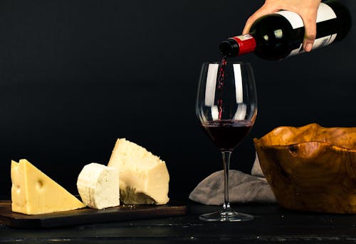Free Photo of Person Pouring Wine into Glass besides Some Cheese Pairings Stock Photo