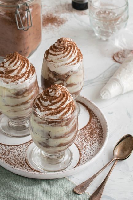 Three creamy tiramisu desserts topped with cocoa powder in elegant glasses.