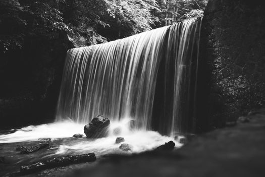 A serene black and white image of a waterfall cascading over rocks with flowing water.
