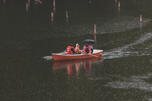 People in a rowboat with life vests, navigating a rainy lake scene.