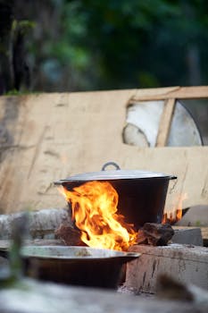 A cooking pot heats over an open flame in a rustic outdoor setting, illustrating traditional outdoor cooking.