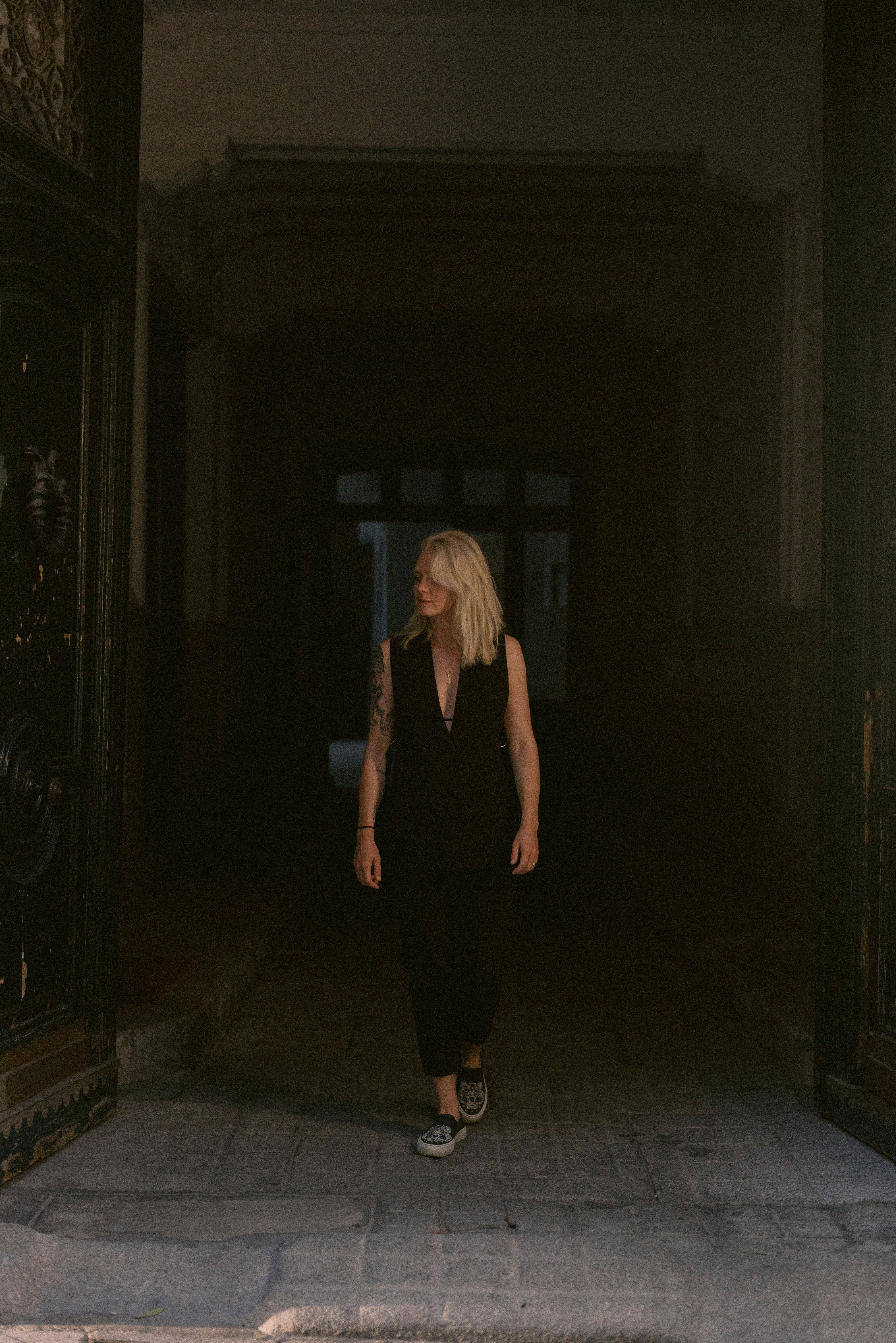 Blonde woman in a black dress walking through a dimly lit hallway, exuding elegance.