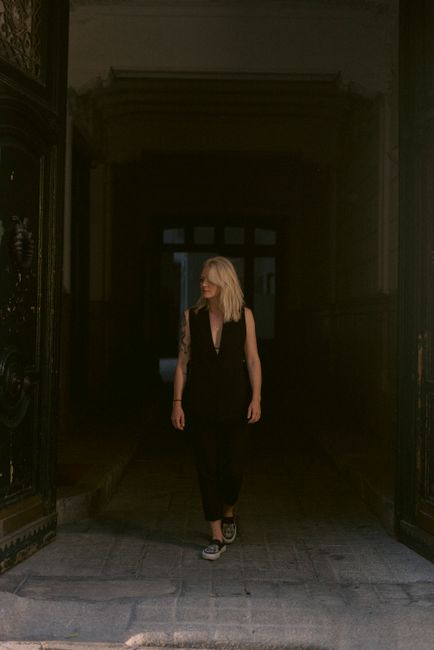 Blonde woman in a black dress walking through a dimly lit hallway, exuding elegance.