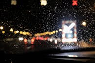 透过被雨水淋湿的挡风玻璃，可以看到夜间模糊的交通景象，灯光闪烁，反射斑驳