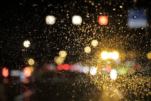Street lights glistening through raindrops on a car window at night, creating a bright bokeh effect.