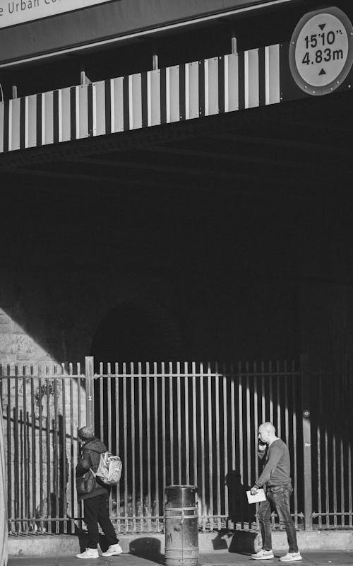 Black and White Photo of People Walking under Bridge