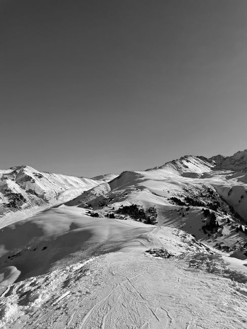 Monochrome aerial view of snow-capped mountain peaks under a clear sky, showcasing winter's beauty.