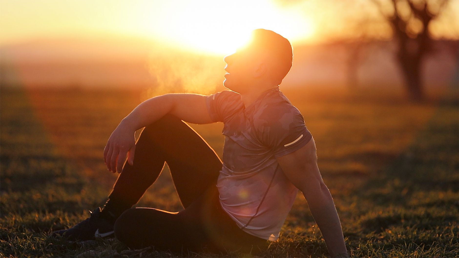 Melanotan 2 cancer benefits — Muscular man sits in rural field at sunset, exhaling visible breath.