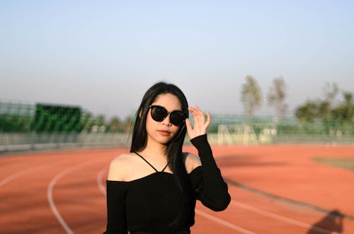 Brunette Woman Wearing Sunglasses Posing against an Orange Sports Field