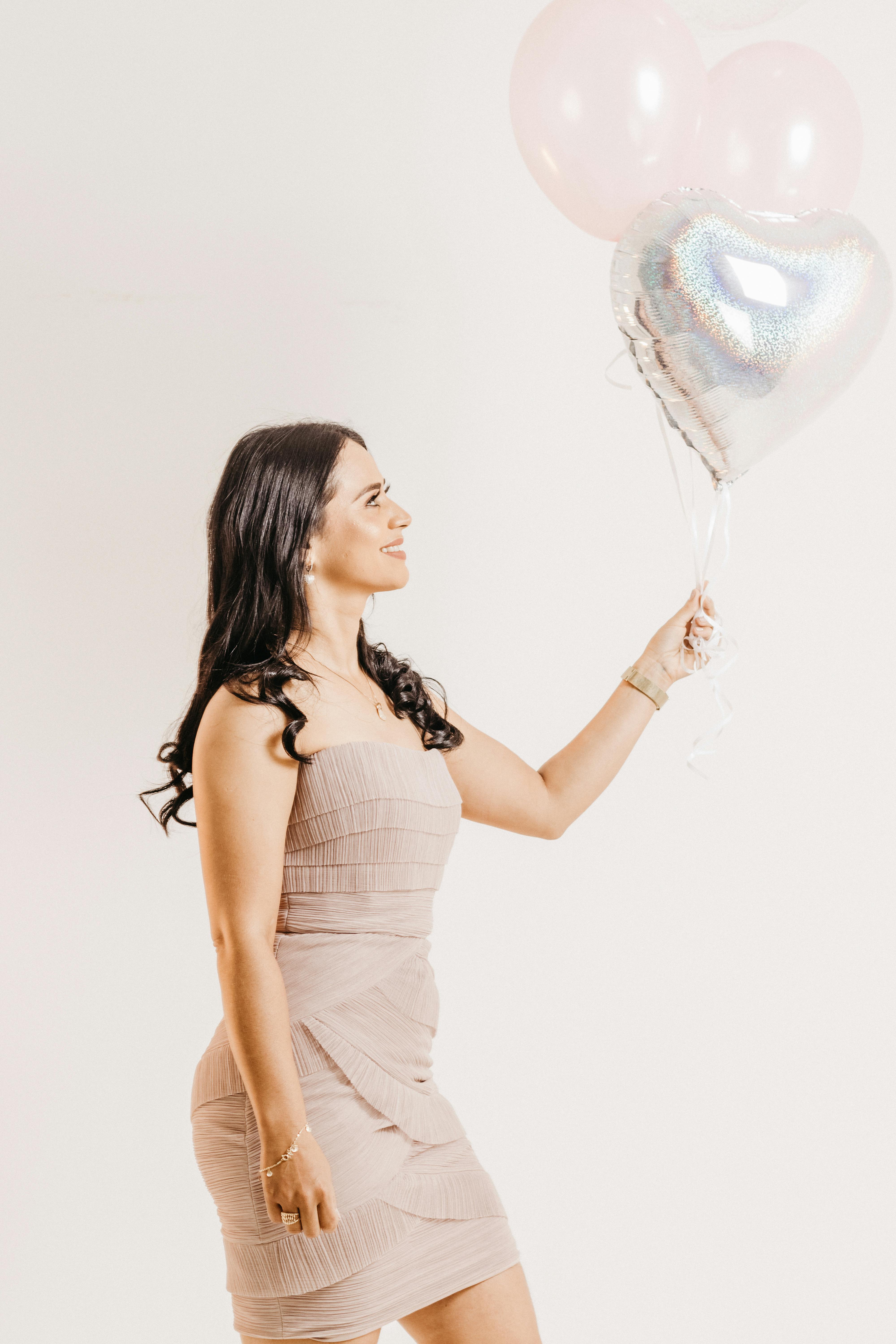 Free Stylish woman posing with balloons in a studio setting, dressed in a sequin dress and smiling. Stock Photo