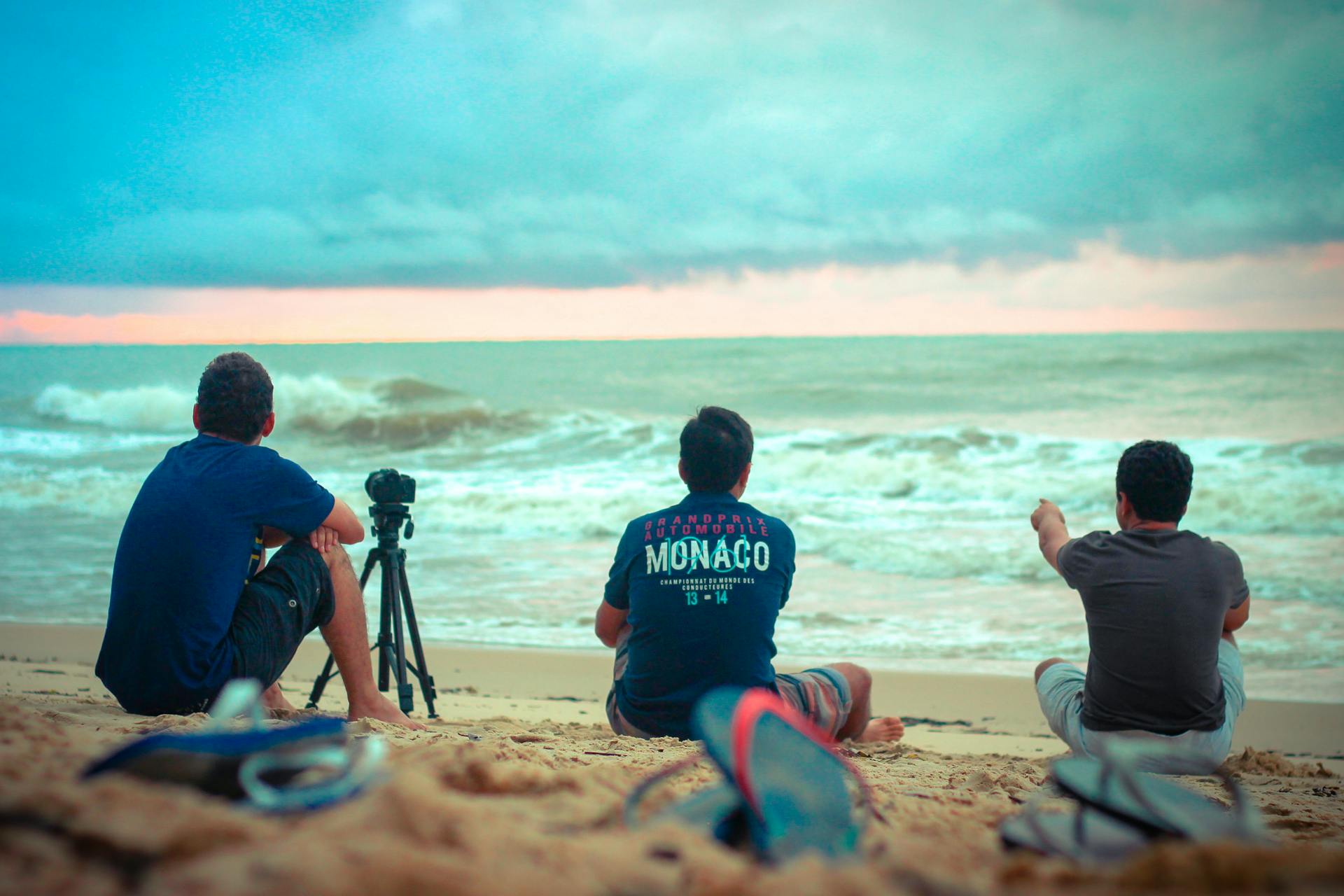 A serene moment on Porto Seguro beach with three men enjoying the sunset by the ocean.