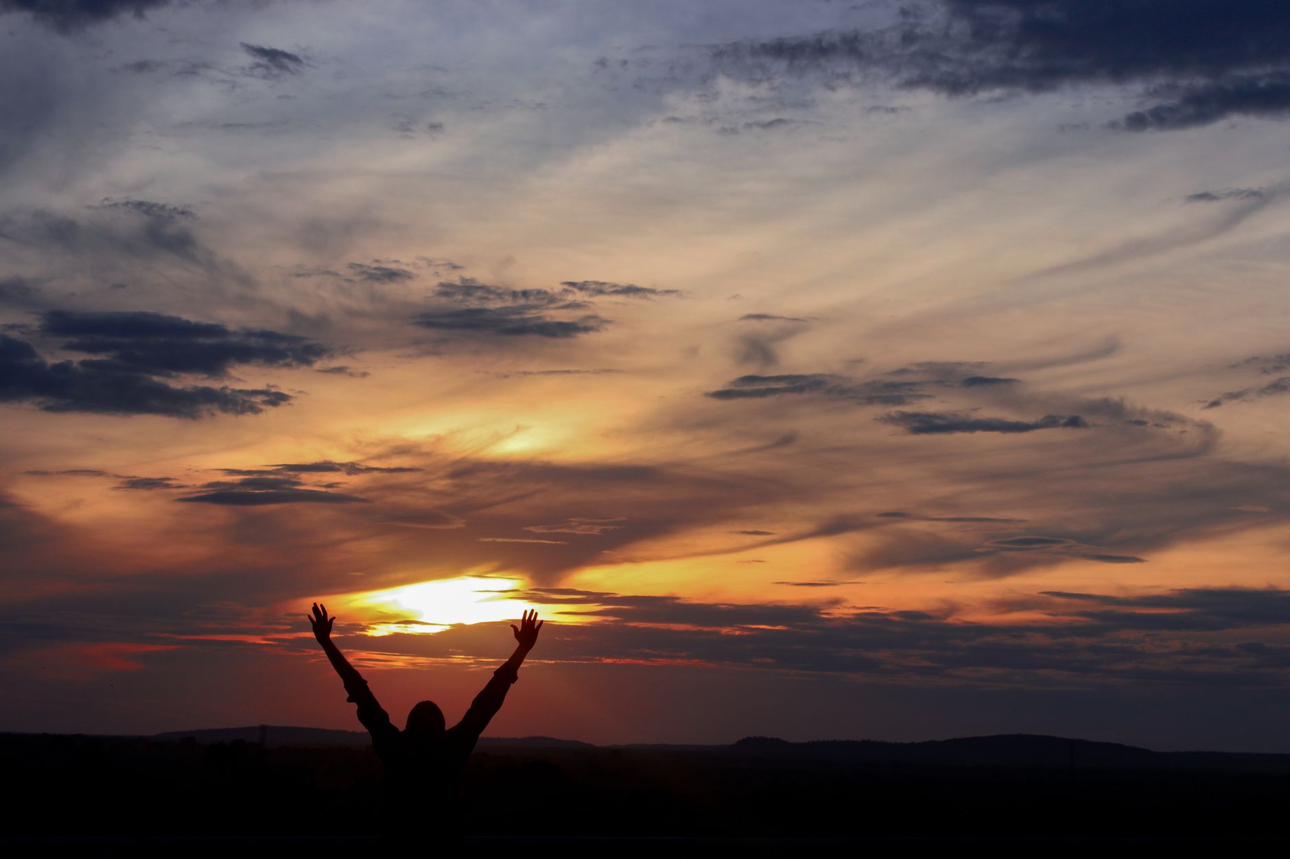 Silhouette of a person with raised arms against a vibrant sunset sky in Brasil.