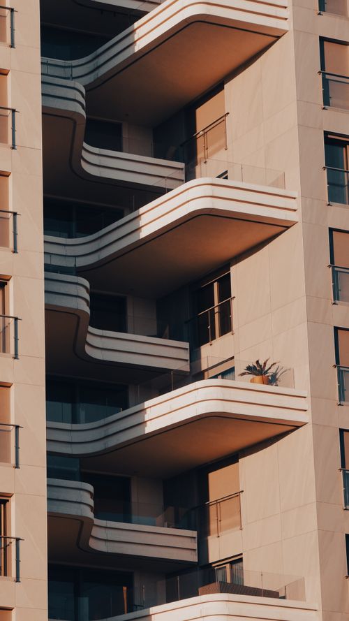 Free Close-up of a modern high-rise building featuring stylish balconies under warm sunlight. Stock Photo