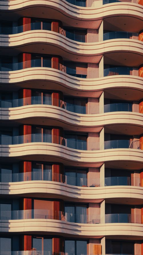 Free Close-up of a modern urban building facade featuring curved balconies in warm sunlight. Stock Photo