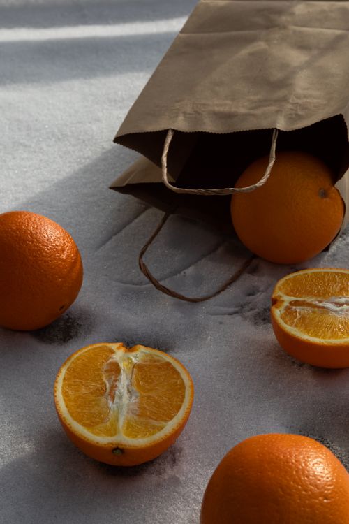 Free Vibrant oranges scattered on snow from a paper bag, capturing a fresh and natural scene. Stock Photo