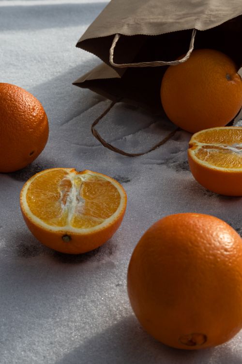 Free Halved and whole oranges on a textured surface with paper bag. Stock Photo