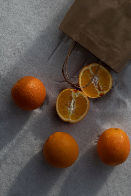 Free Top view of fresh oranges and a paper bag on a sandy beach, emphasizing summer vibes. Stock Photo