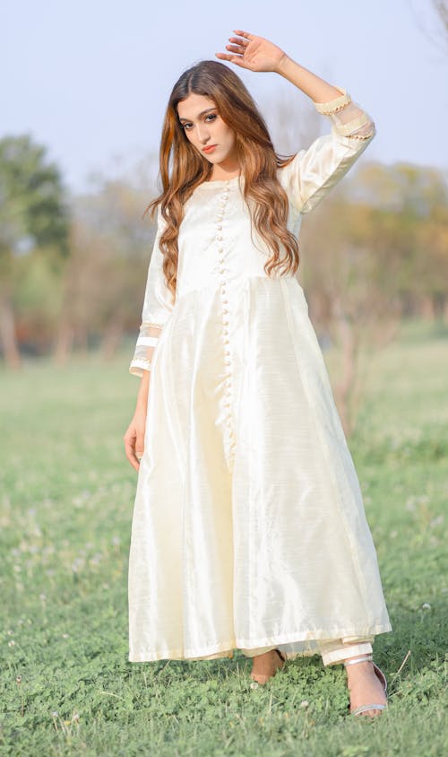 Woman in White Dress Standing with Arm Raised on Meadow