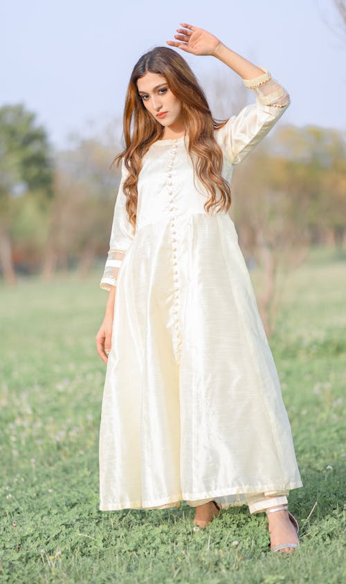 Free Woman in White Dress Standing with Arm Raised on Meadow Stock Photo