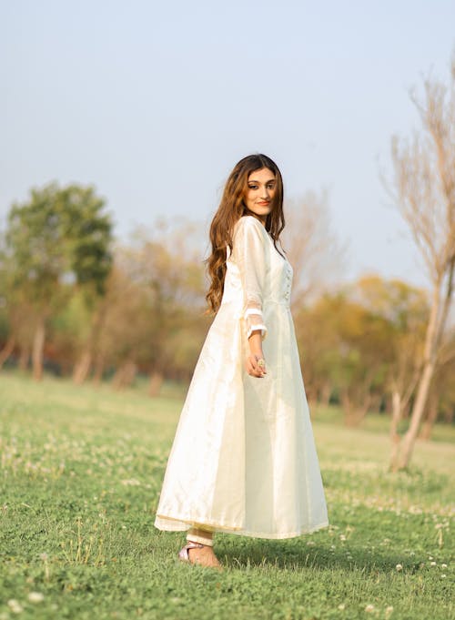 A Woman in White Dress Standing on Green Grass Field