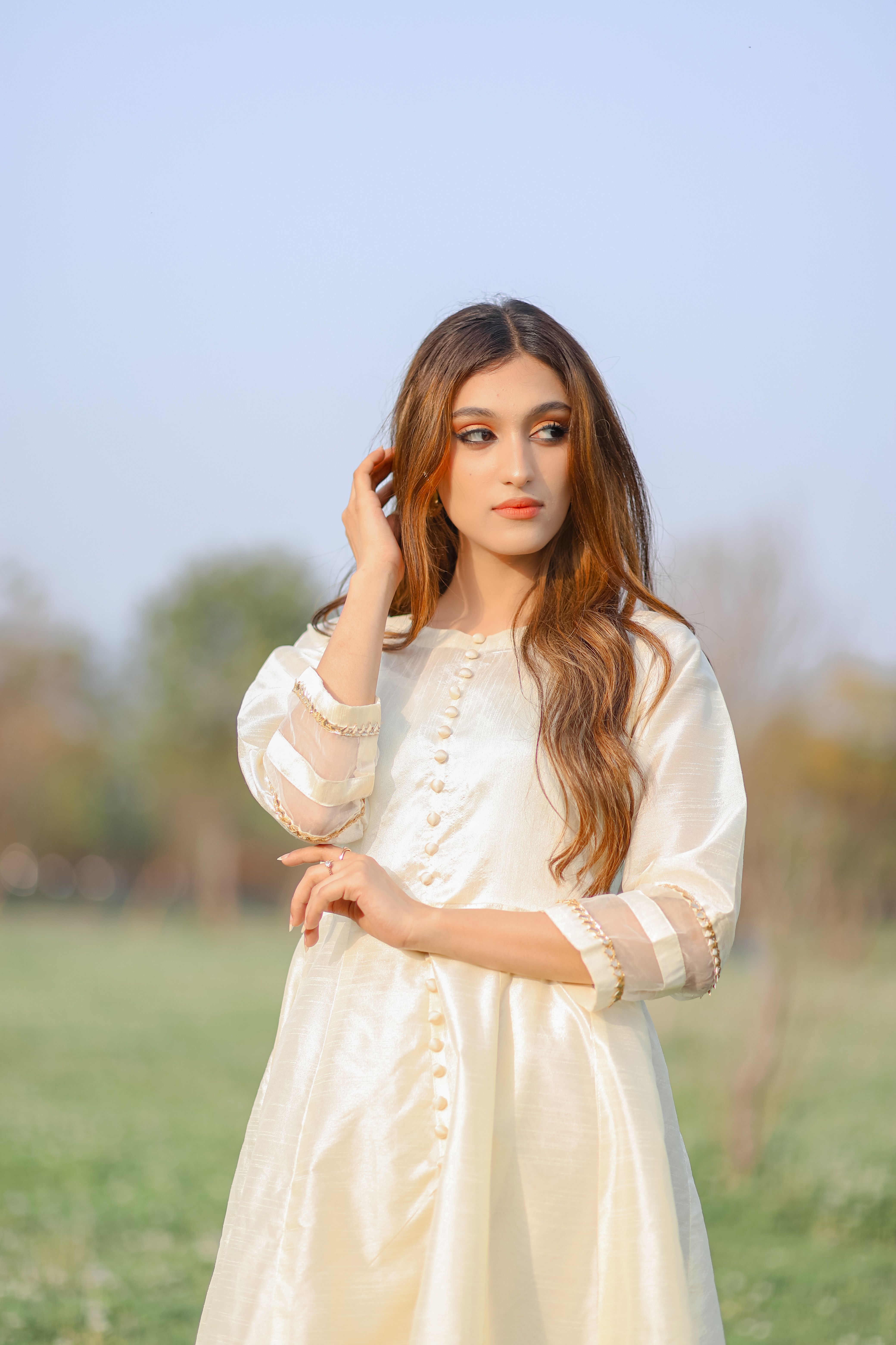 Portrait of a woman in a white dress standing in a serene rural landscape.