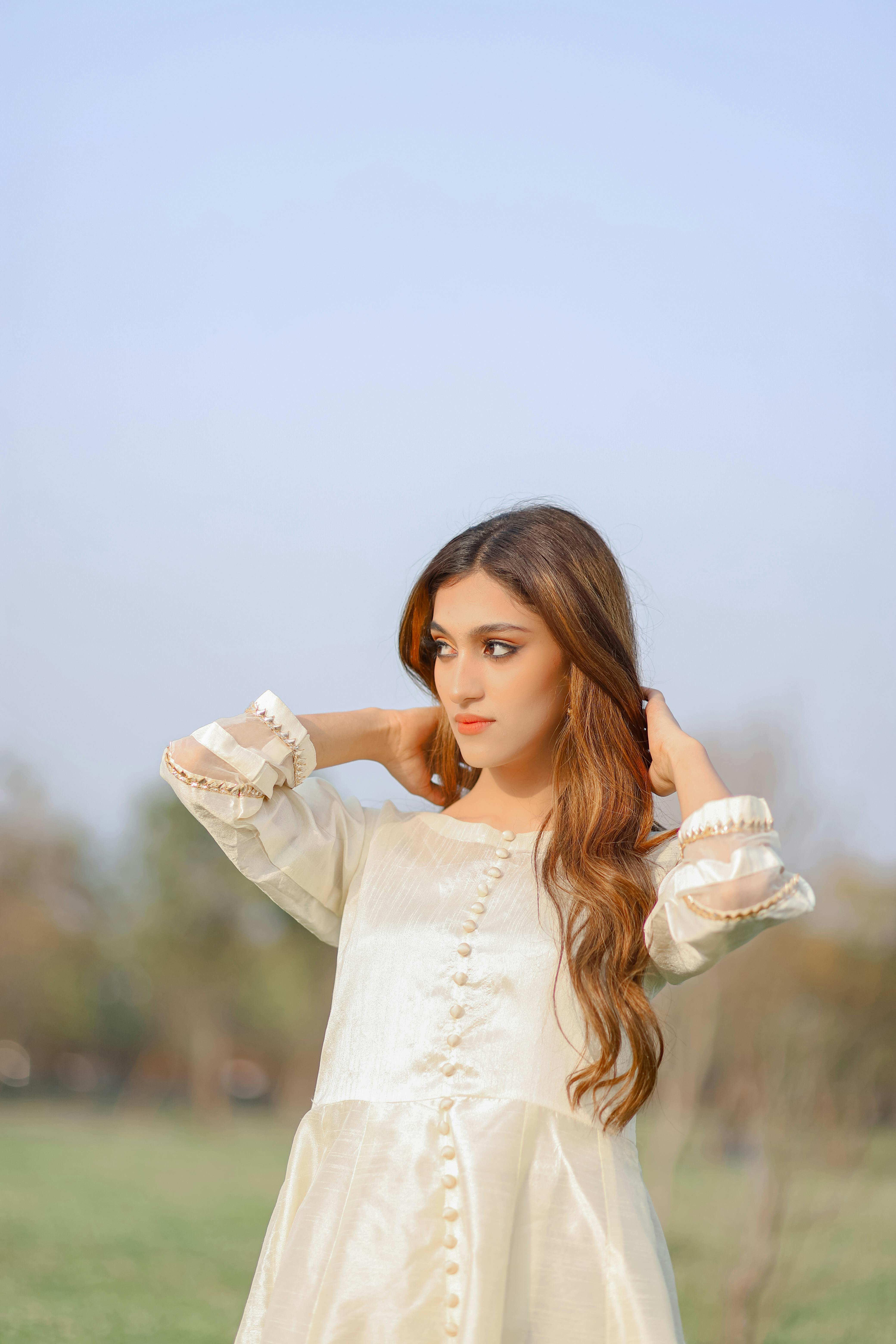 Elegant woman in a white dress posing outdoors on a sunny day, showcasing fashion and style.
