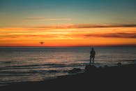 迷人的日落中，一架无人机飞越波罗的海，岸上有一个人的剪影