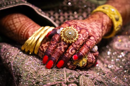 Free Close-up of beautifully hennaed hands adorned with traditional gold jewelry and vibrant fabrics. Stock Photo