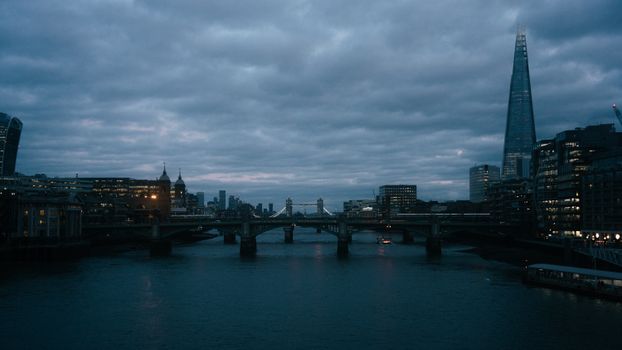 Dramatic evening view of London cityscape with The Shard and bridge over the Thames River.