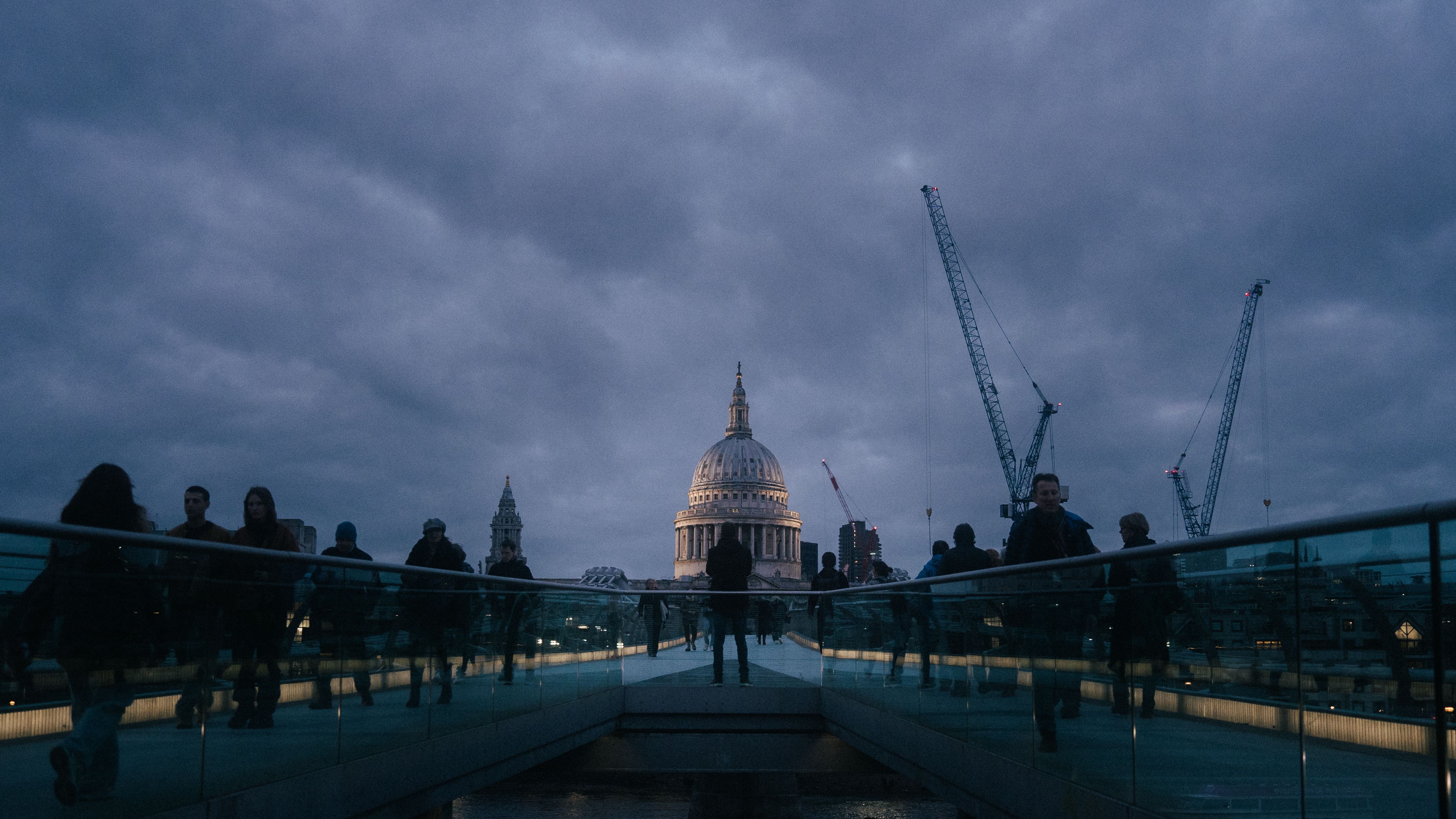 Dramatic view of St. Paul's Cathedral from Millennium Bridge at dusk with silhouetted pedestrians.