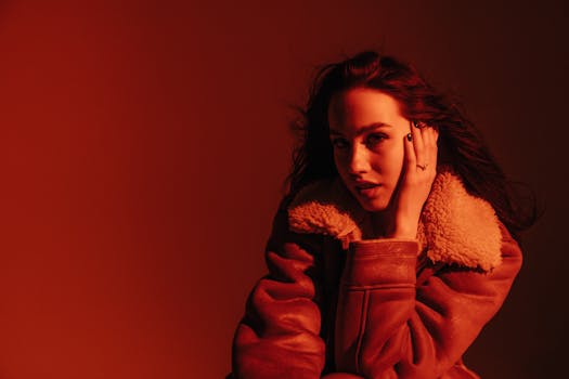 A striking portrait of a woman in a shearling jacket with shadow and red lighting.