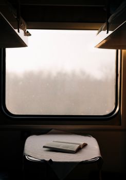 A peaceful train compartment with an open book on a table, showcasing a serene window view.
