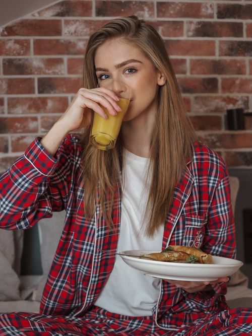 Free A woman in plaid pajamas enjoying breakfast with orange juice indoors. Stock Photo