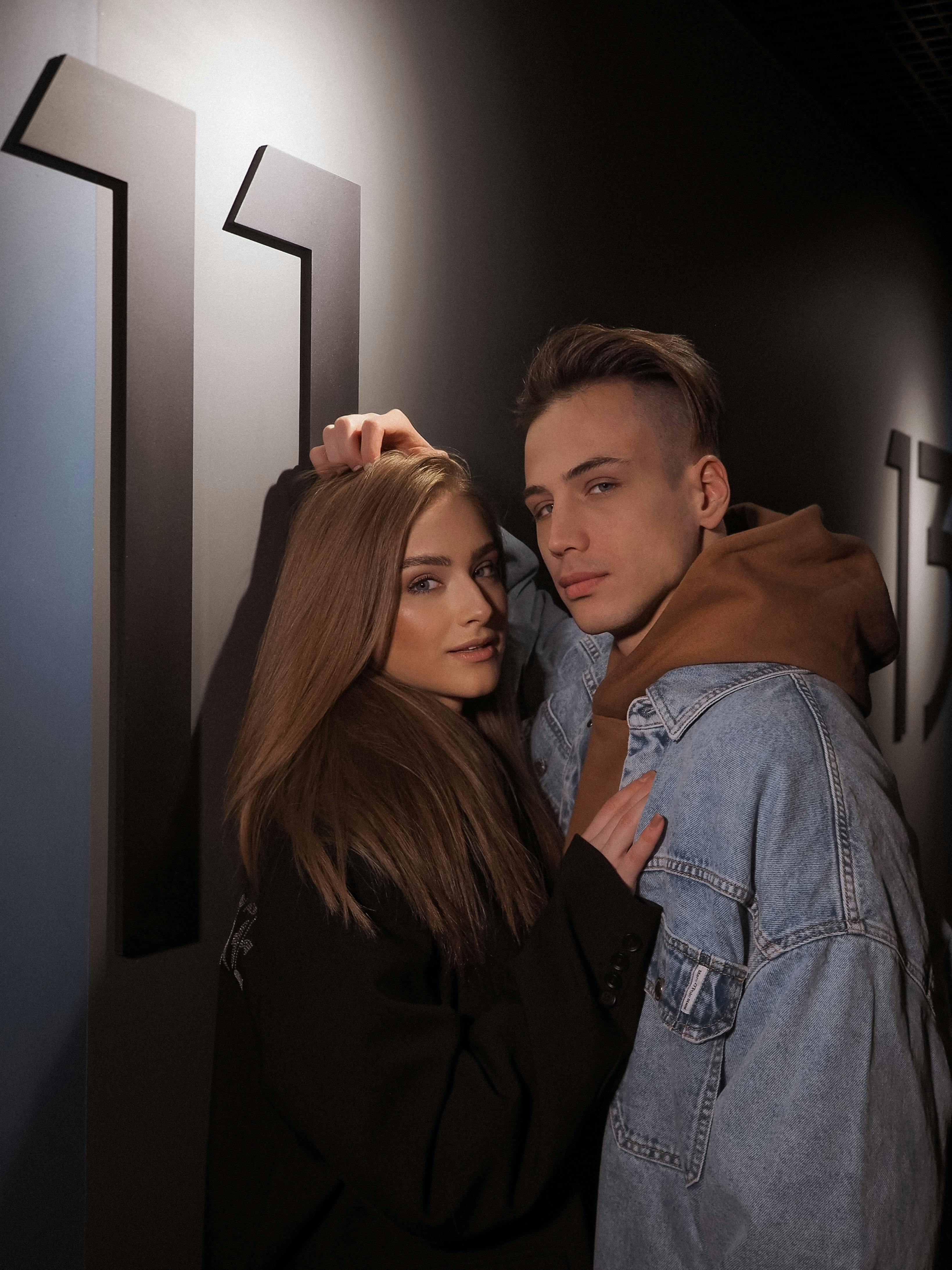 Fashionable couple posing together against a modern, dark backdrop indoors.