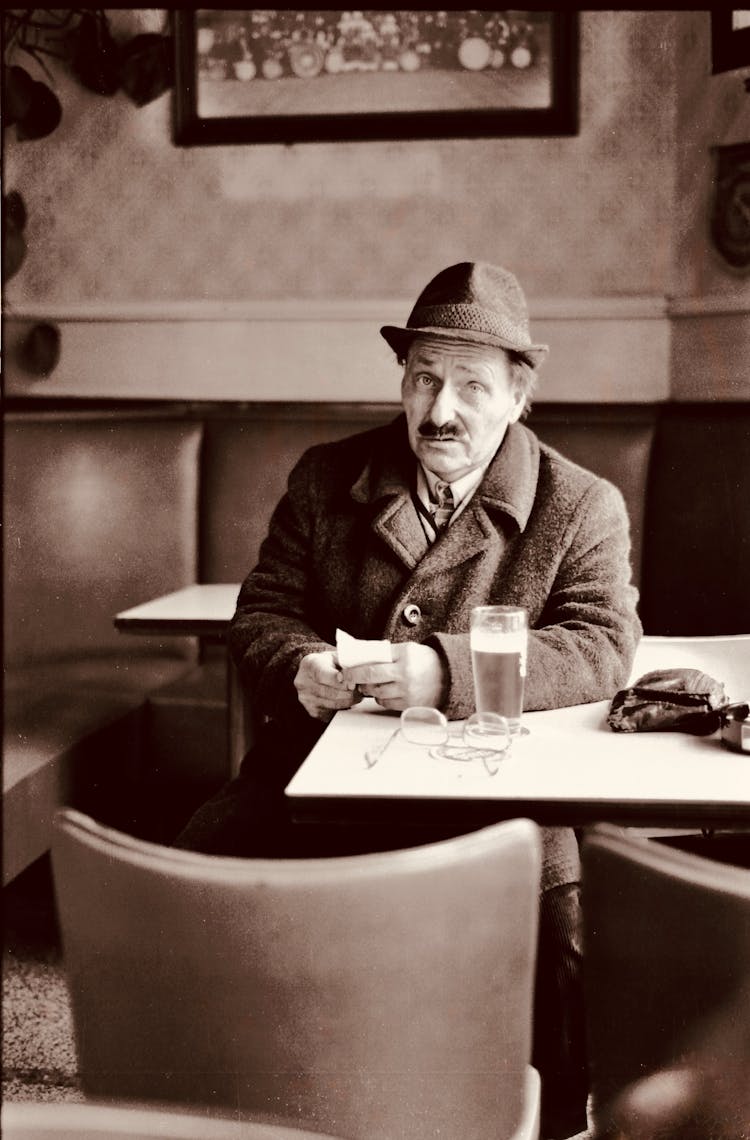 Elderly Man In Coat And Hat Sitting At Cafe