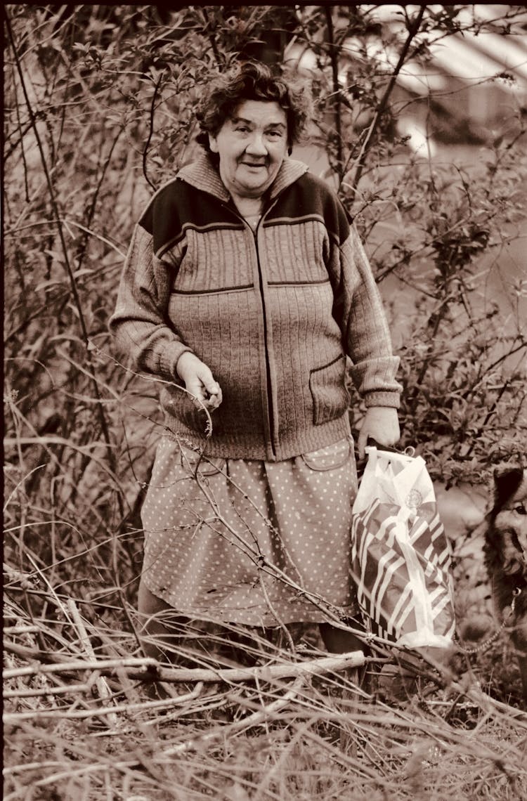 Elderly Woman With Bag Among Bushes