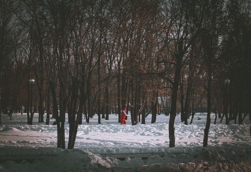 Santa Claus walks through a snowy forest, surrounded by trees in a serene winter scene.