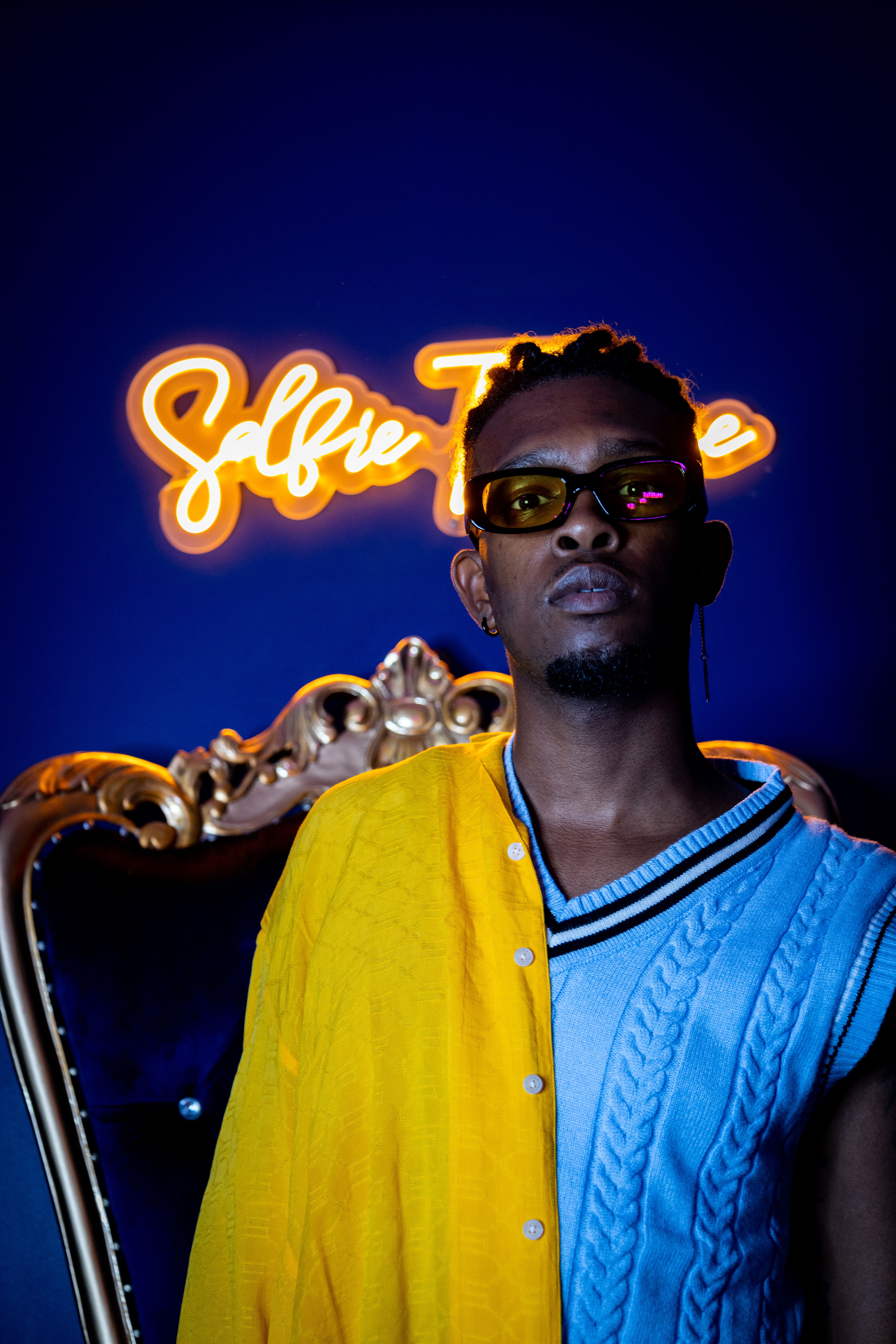 Fashionable model in yellow and blue attire posing with neon background lighting.