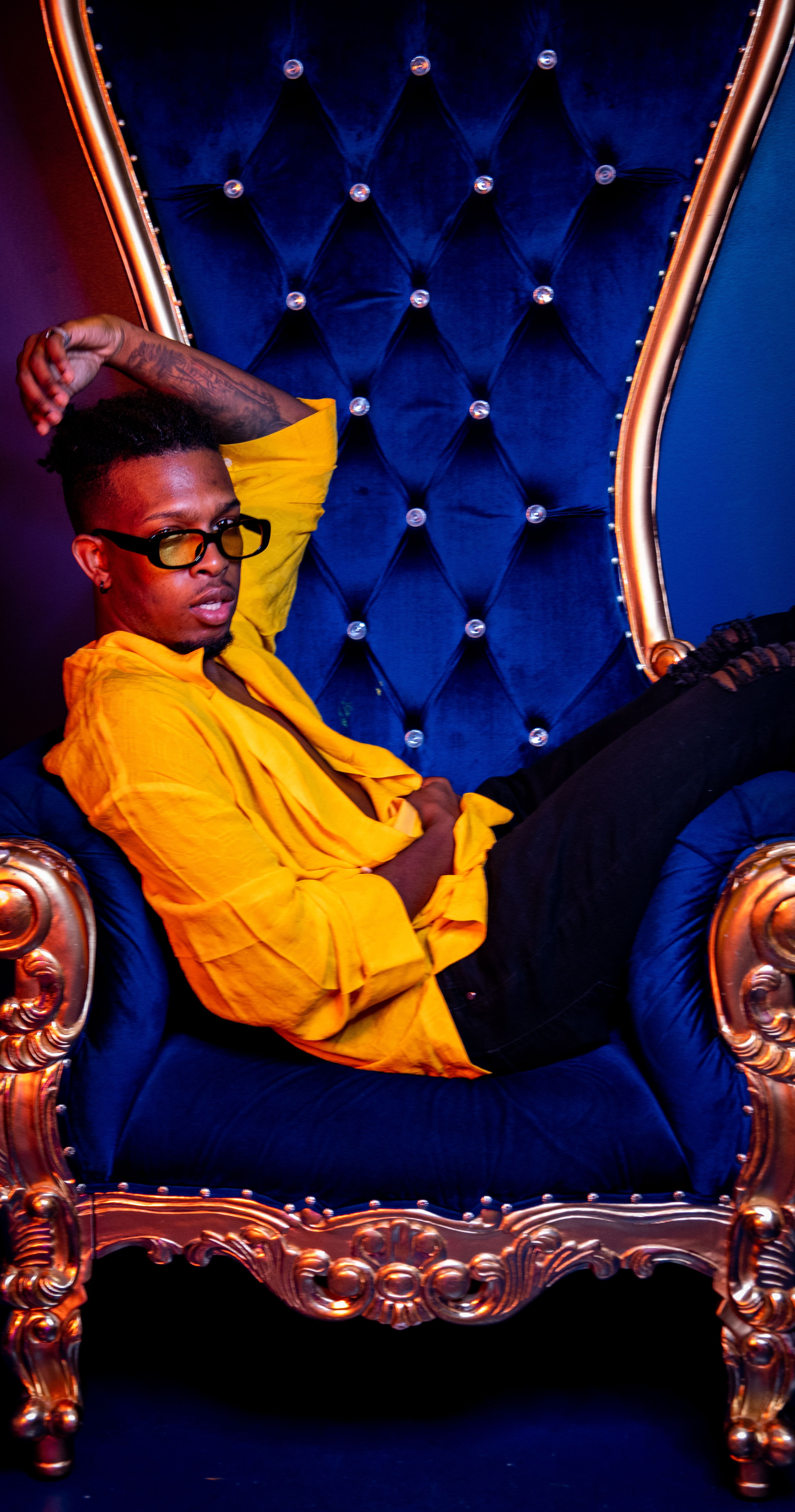 Fashionable adult posing on an ornate blue chair, showcasing luxury and style.